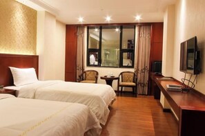 Habitación de hotel con dos camas, televisión, una mesita con sillas y ventana con cortinas.