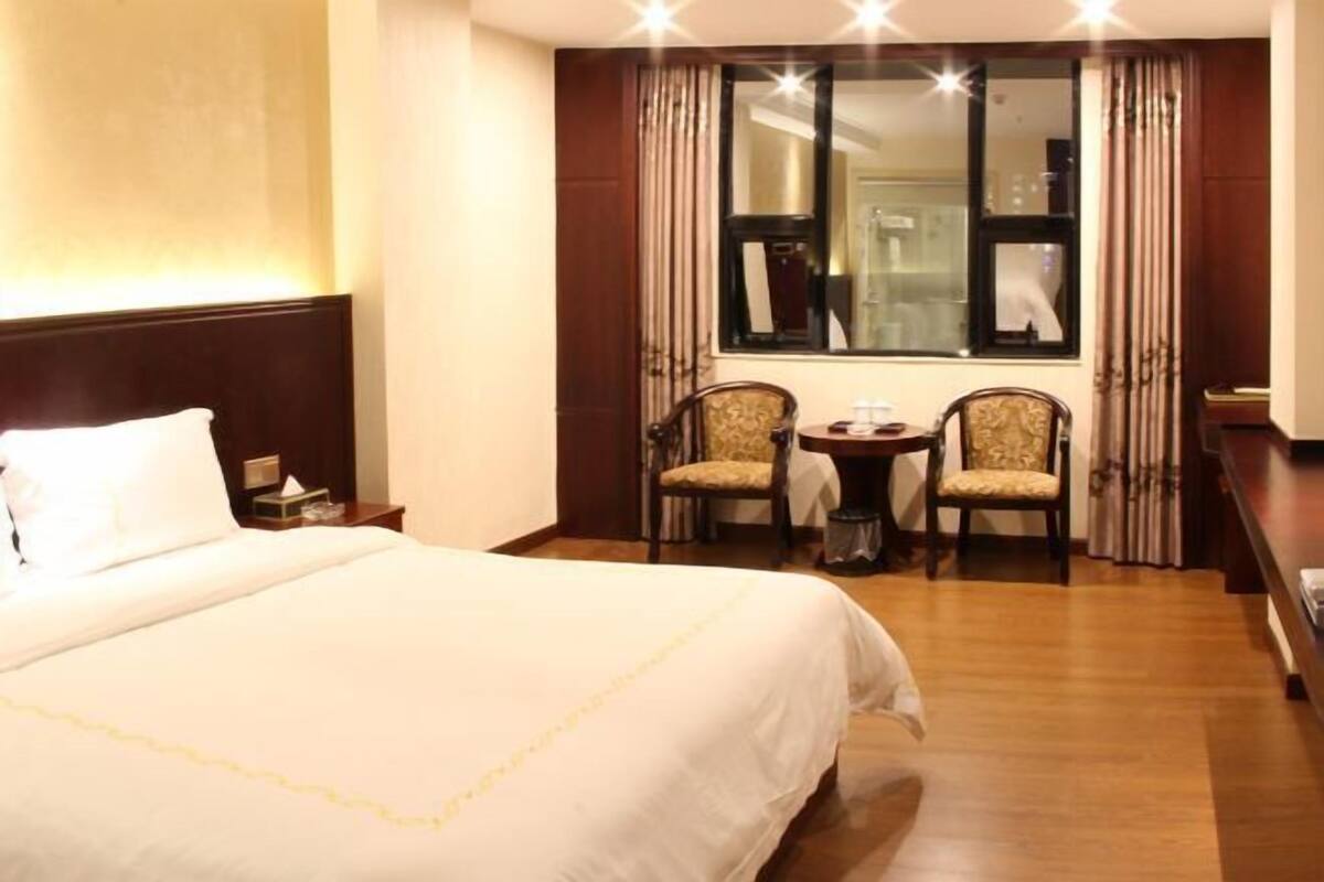 Ein Hotelzimmer mit einem großen Bett, zwei Sesseln, einem kleinen Tisch und einem Fenster mit Vorhängen.