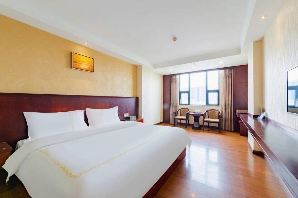 Ein Hotelzimmer mit einem großen Bett, einem Schreibtisch und einem Stuhl. Ein Fenster mit Vorhängen und ein Bild an der Wand sind ebenfalls vorhanden.