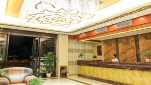 Zona de recepción de un hotel con mostrador de mármol, candelabro y plantas en macetas.