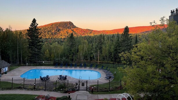 Une piscine dotée de chaises longues et offrant une vue sur une colline boisée.