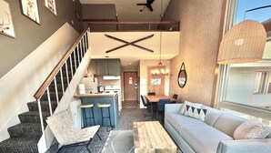 Un salon moderne avec un escalier, un coin repas et une cuisine en arrière-plan.