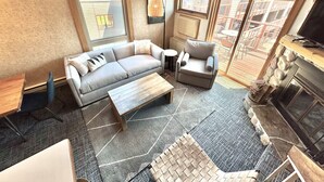 Un salon moderne comprenant un canapé, un fauteuil, une table basse, une cheminée et de grandes fenêtres.