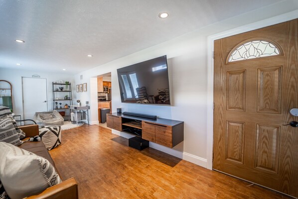 A modern living room with a flat-screen TV mounted on a wooden console, hardwood flooring, and a large wooden door with a glass panel. - Beautiful Oasis Home, Walking Distance to Ray Jay (Tampa)