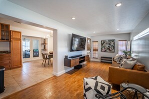 A spacious living area with a wooden floor, a television, a sofa, and a dining table. - Beautiful Oasis Home, Walking Distance to Ray Jay (Tampa)