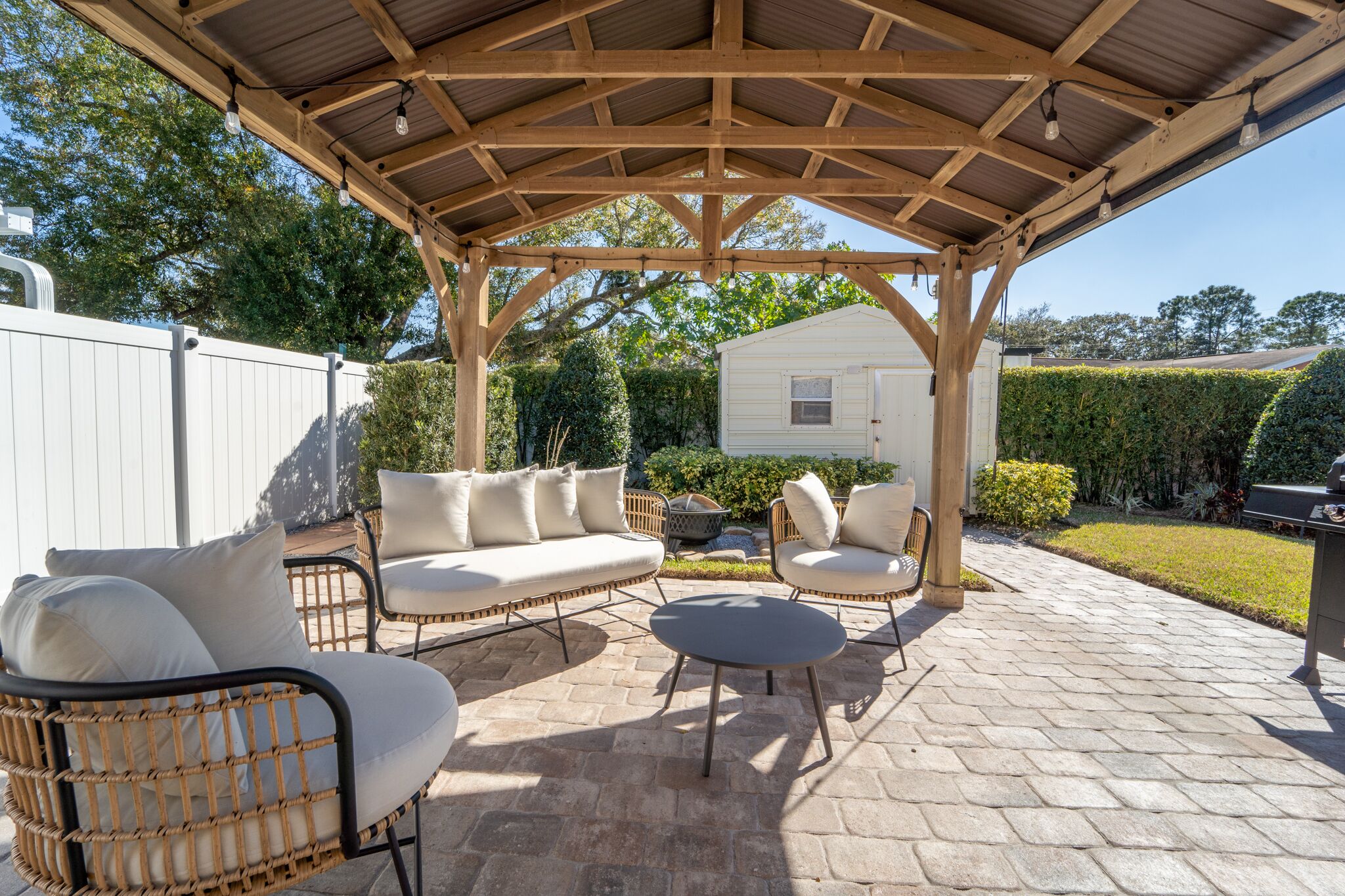 An outdoor patio with a wooden pergola, wicker furniture, and a stone floor.