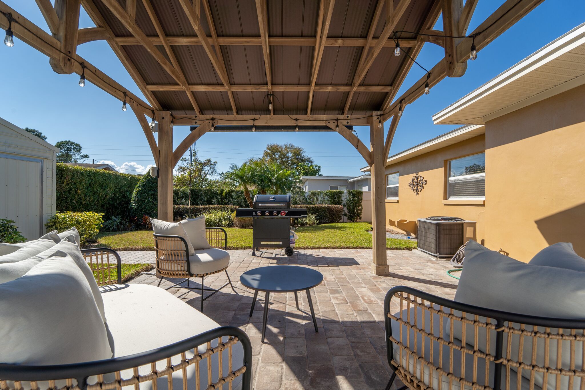 An outdoor patio with a pergola, seating area, and a barbecue grill.