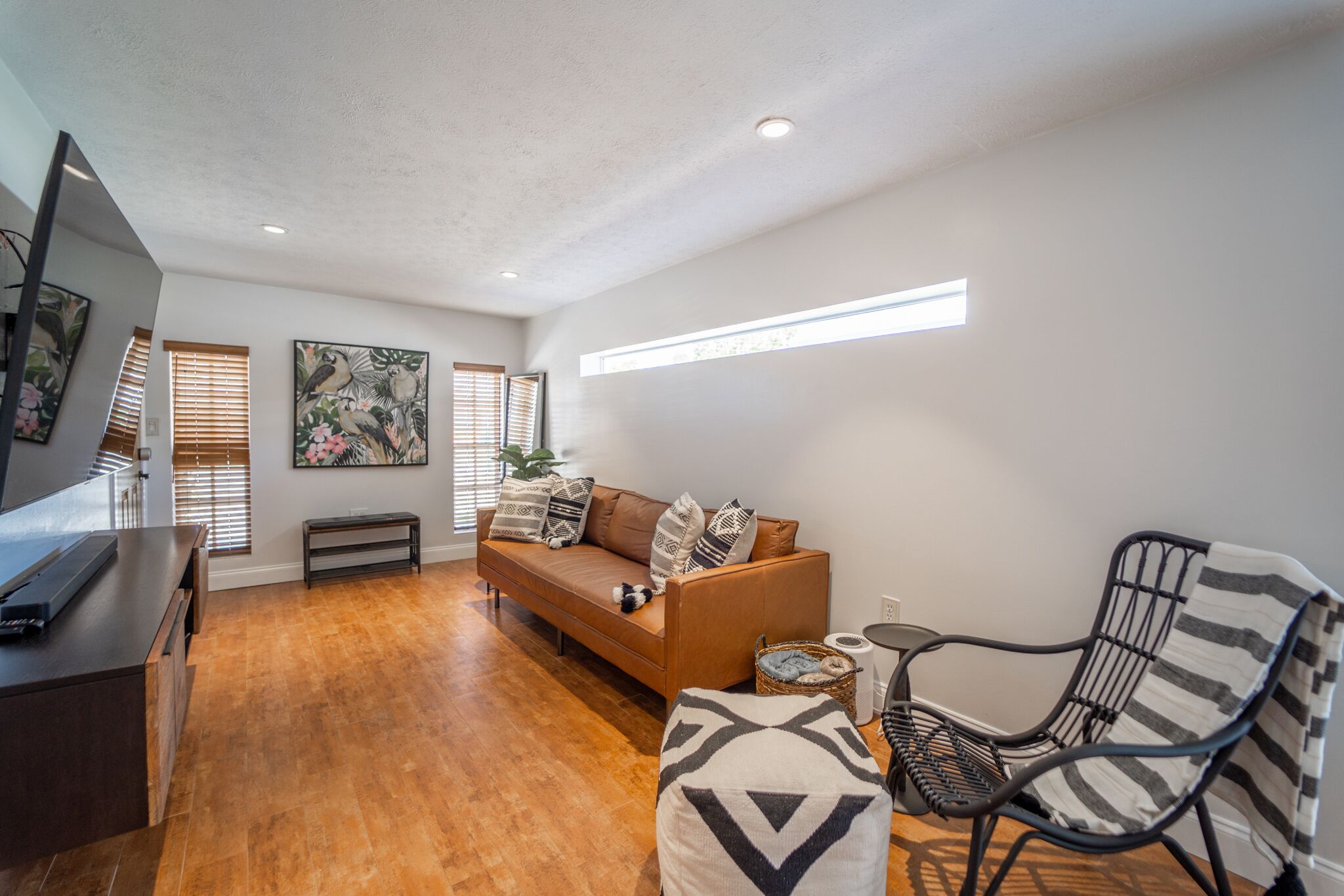 Un salon moderne avec un plancher en bois, un canapé marron, un fauteuil à rayures noires et blanches, et un téléviseur à écran plat posé sur un meuble en bois.