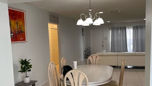 A dining area with a round table, six chairs, a potted plant, and a painting on the wall. - A Great Boca Home Stay (Boca Raton)