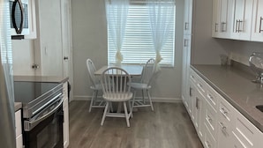 A modern kitchen with white cabinets, a built-in oven, and a dining area with a table and chairs. - A Great Boca Home Stay (Boca Raton)