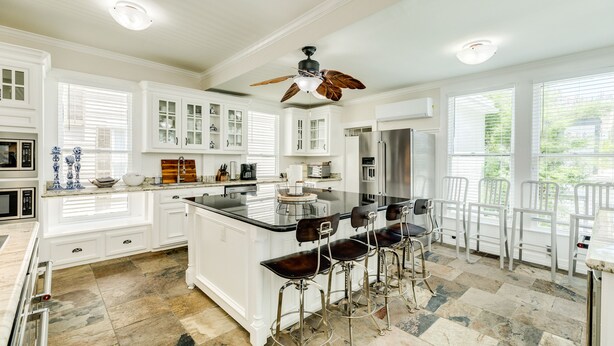 A spacious kitchen with white cabinetry, a central island with bar stools, and a ceiling fan.