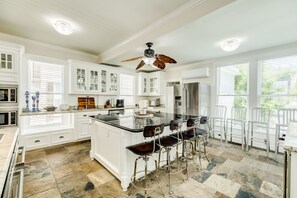 A spacious kitchen with white cabinetry, a central island with bar stools, and a ceiling fan.