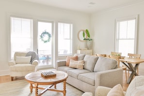 A living room with a beige sofa, a round wooden coffee table, and a dining area with a wooden table and chairs.