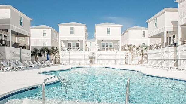A swimming pool surrounded by white buildings with balconies and lounge chairs. - The Sand Haus - Steps to Beach - 7 Separate Beds - Pet Friendly - Pool - Grill (Gulf Shores)