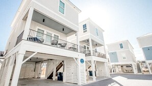 A multi-story building with balconies and a covered parking area. - The Sand Haus - Steps to Beach - 7 Separate Beds - Pet Friendly - Pool - Grill (Gulf Shores)