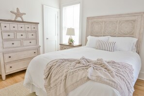 Un dormitorio con una cama grande, un aparador con cajones, una mesita de noche con lámpara y una decoración con forma de estrella de mar.