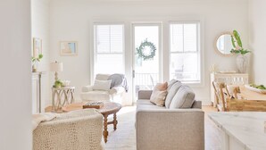 A bright, white living room with a sofa, armchairs, a coffee table, and a dining area. - The Sand Haus - Steps to Beach - 7 Separate Beds - Pet Friendly - Pool - Grill (Gulf Shores)
