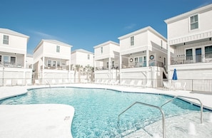 A swimming pool surrounded by white buildings with balconies, clear blue sky, and no visible people.