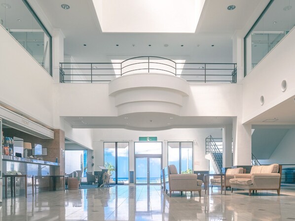 A spacious lobby with a high ceiling, a central staircase, and a view of the ocean.