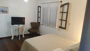 A small, simple room with a bed, a chair, a table with a television, and a window with curtains. - Pousada Arvore Da Vida (Teresópolis)