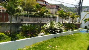 A residential garden with various plants and a white fence. - Pousada Arvore Da Vida (Teresópolis)