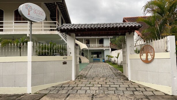 A gated entrance to a property with a signboard, a paved pathway, and a covered walkway leading to a building. - Pousada Arvore Da Vida (Teresópolis)