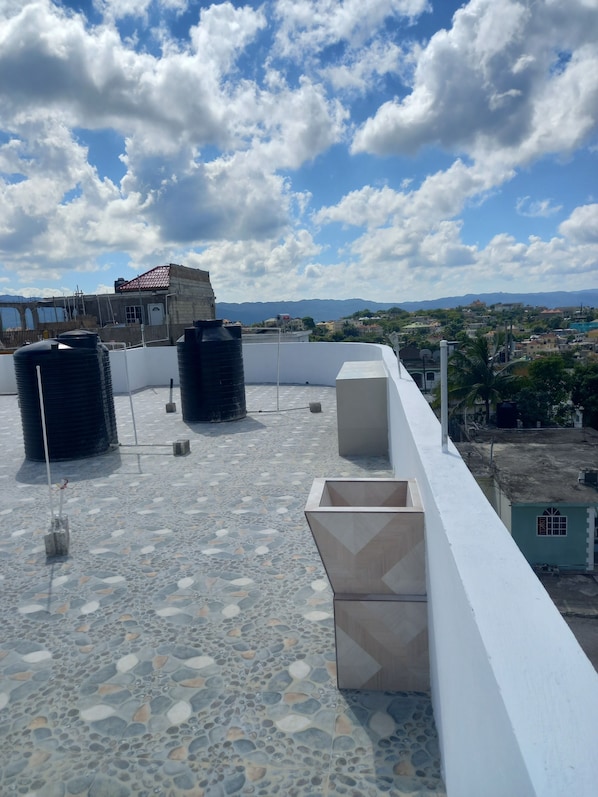 Eine Dachterrasse mit Wassertanks, Blick auf eine Stadtlandschaft und entfernte Berge.