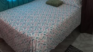 Een slaapkamer met een bed, een kussen, een ingelijste foto aan de muur en gordijnen.