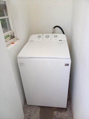 Eine kompakte, weiße Whirlpool Waschmaschine in einem kleinen Waschraum mit Fenster und Schlauch.