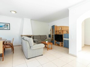 A living room with a sofa, a TV, and a dining area with chairs and a table.