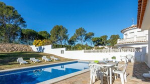 A swimming pool with lounge chairs and a table, surrounded by a white wall and trees. - Beautiful private villa for 6 guests with WIFI, private pool, TV and pets allowed (L'escala)
