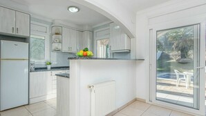A modern kitchen with white cabinetry, a built-in island, and a view of a pool through a glass door. - Beautiful private villa for 6 guests with WIFI, private pool, TV and pets allowed (L'escala)