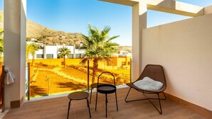 Uma varanda com vista para uma colina, duas cadeiras e uma mesa pequena.