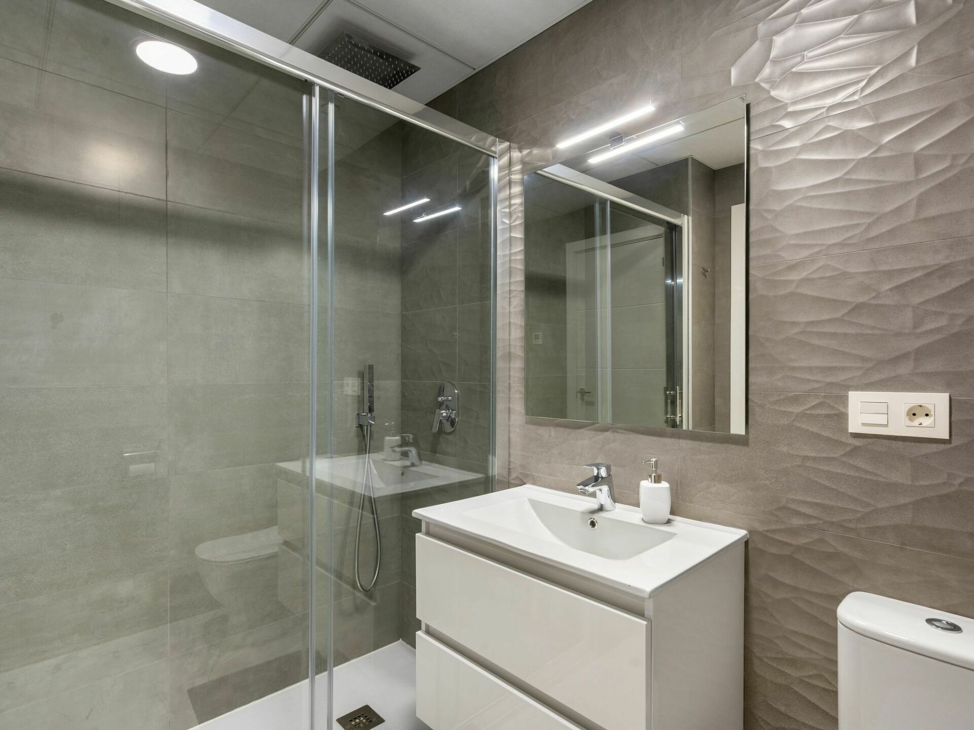 Een moderne badkamer met een douchecabine van glas, een wit wastafelmeubel met spiegel en een wand met structuur.