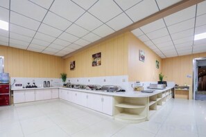 Une cuisine spacieuse avec des meubles blancs, un long comptoir et un plafond carrelé.
