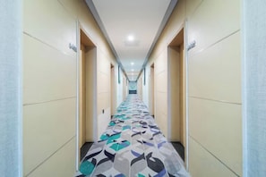 Un couloir d’hôtel avec un sol à motifs, des portes des deux côtés et un luminaire au plafond.