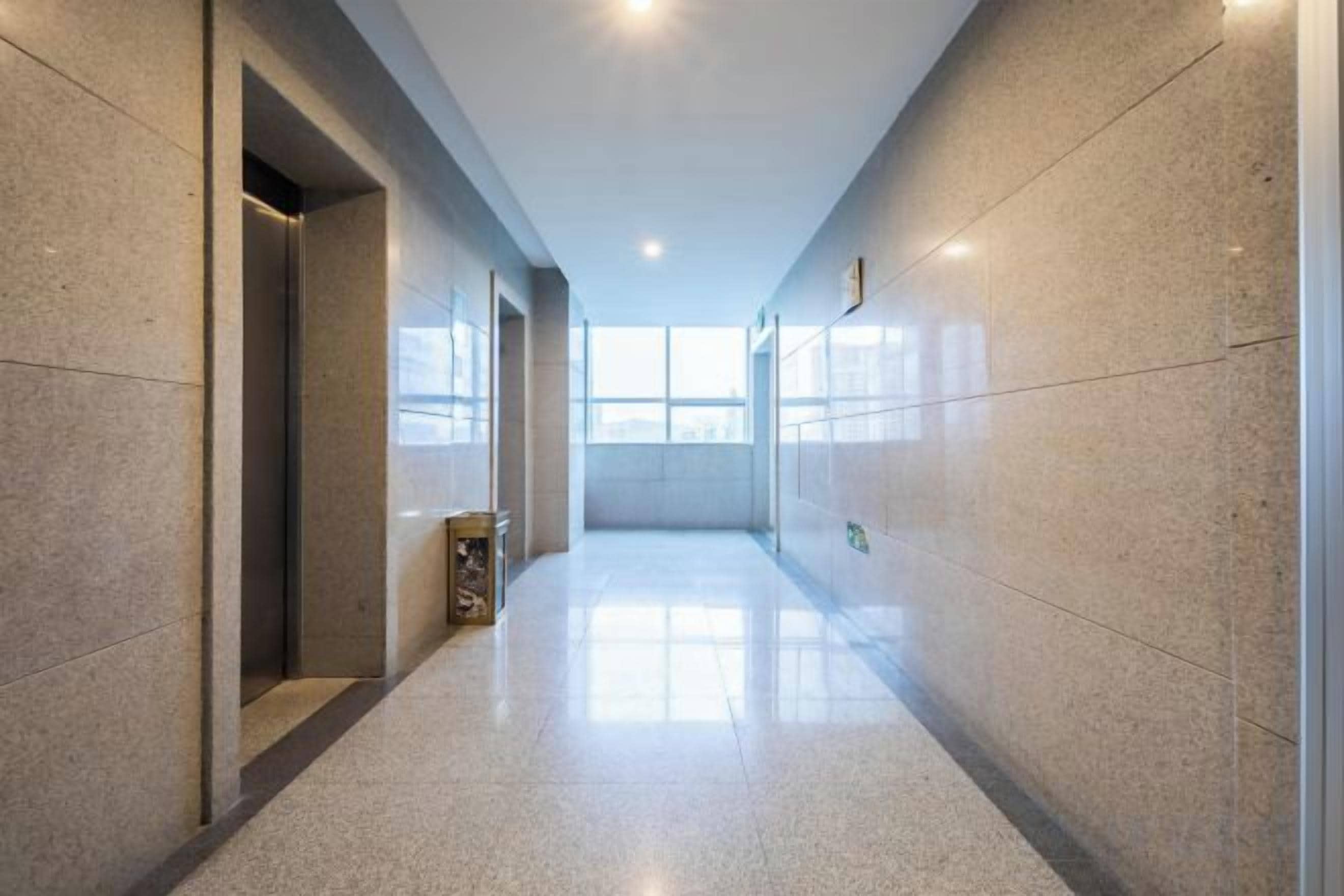 A corridor with a polished floor, a trash bin, and a door on the left.