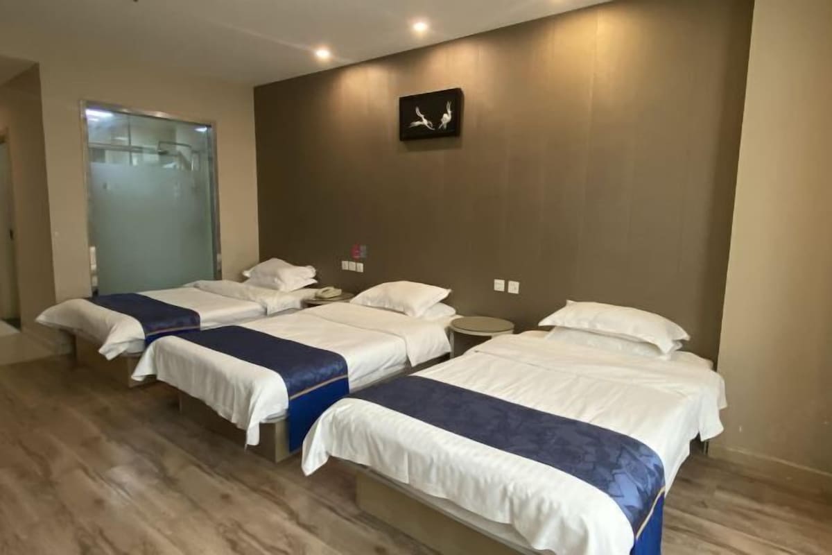 A hotel room with four single beds, a large window, a wall clock, and a small round table.