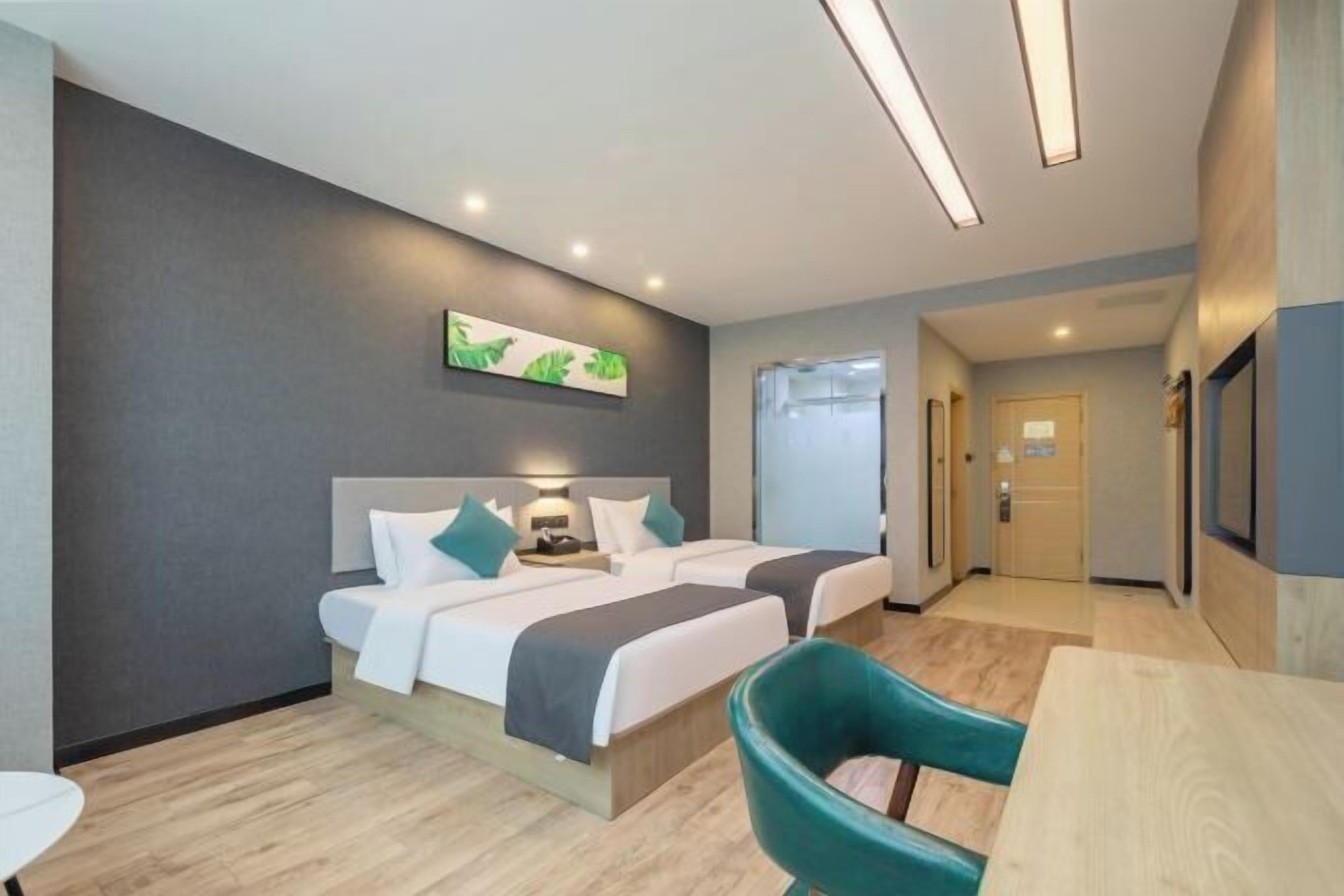 A hotel room with two beds, a desk, and a chair. There is a painting on the wall and a door leading to another room.