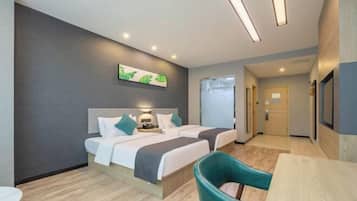 A hotel room with two beds, a desk, and a chair. There is a painting on the wall and a door leading to another room.