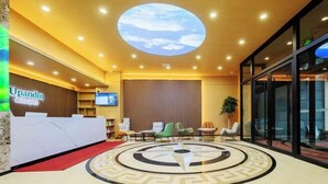 Un espace d’accueil d’hôtel au design moderne, comprenant un comptoir d’accueil, un espace salon et un grand motif décoratif circulaire sur le sol.