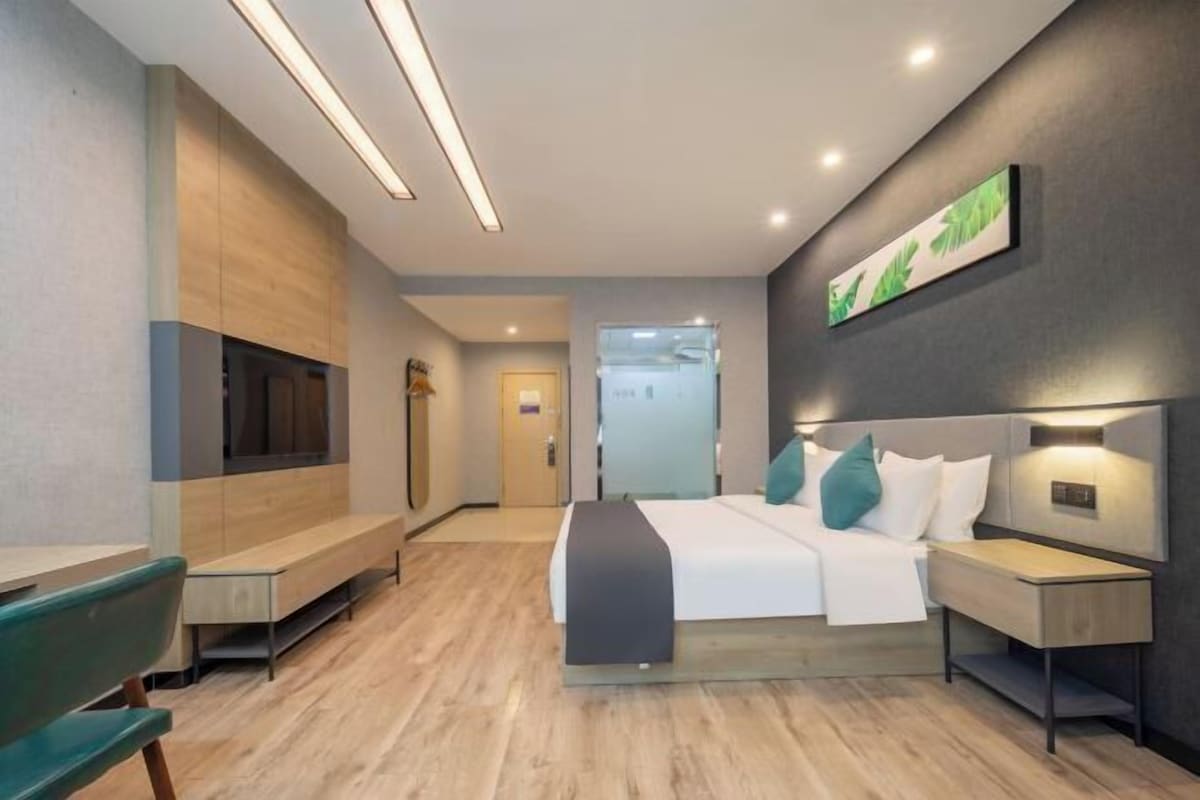 A modern hotel room with a bed, bedside tables, a bench, and a wall-mounted TV.