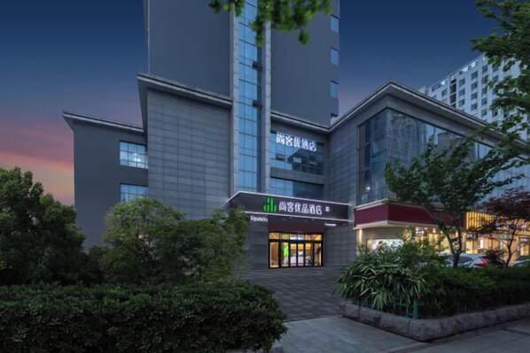 En modern hotellbyggnad med en framträdande entré, stora fönster och ett välskött trädgårdsområde.