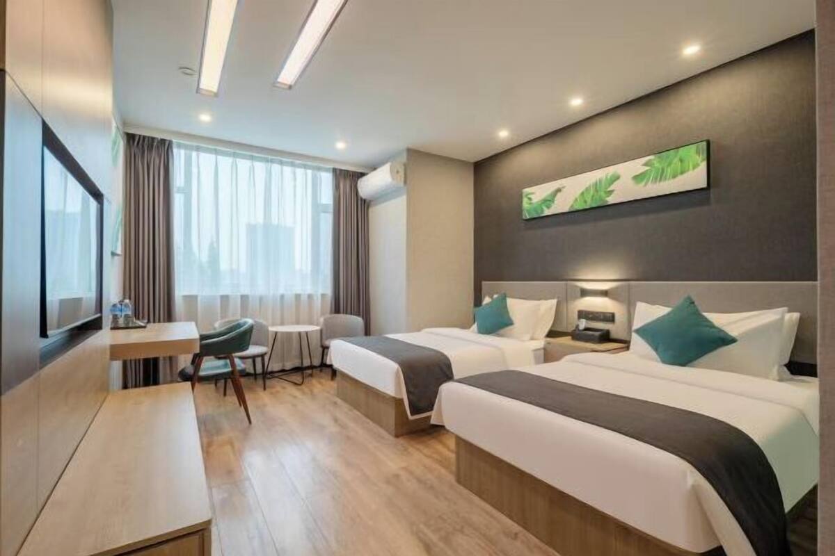 Habitación de hotel con dos camas, un escritorio, una silla y un ventanal con cortinas.