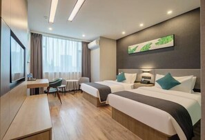 Ein Hotelzimmer mit zwei Betten, einem Schreibtisch, einem Stuhl und einem großen Fenster mit Vorhängen.