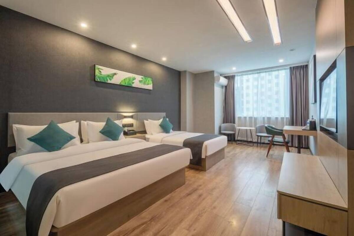 Habitación de hotel con dos camas, un escritorio, una silla y un amplio ventanal con cortinas.