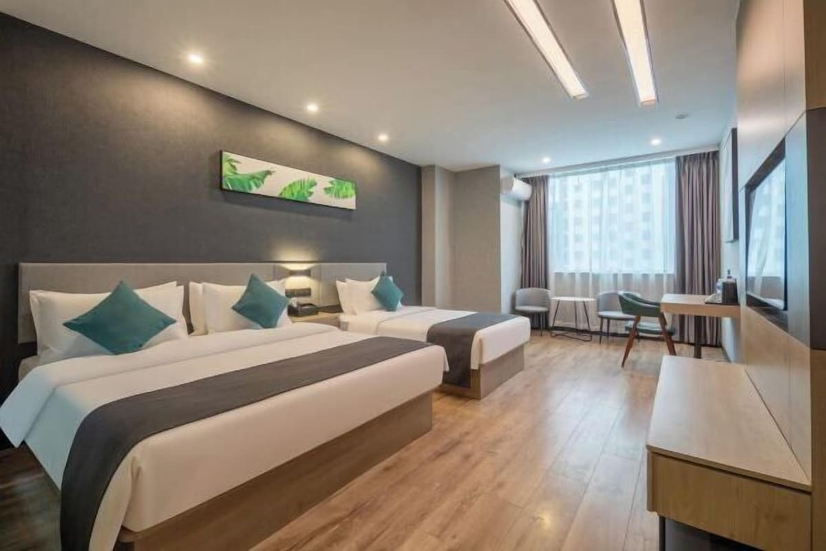 A hotel room with two beds, a desk, a chair, and a large window.