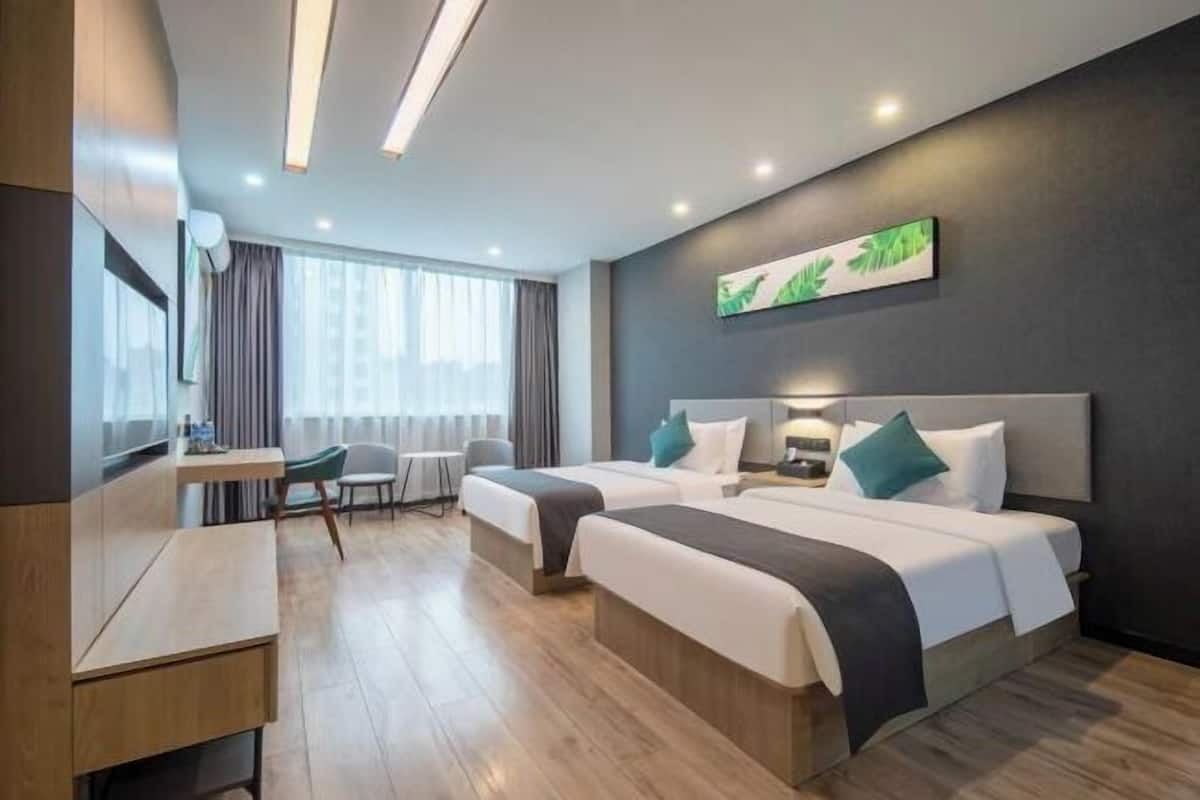 Habitación de hotel con dos camas, un escritorio y una silla. Hay una ventana con cortinas, un cuadro en la pared y una lámpara en el techo.