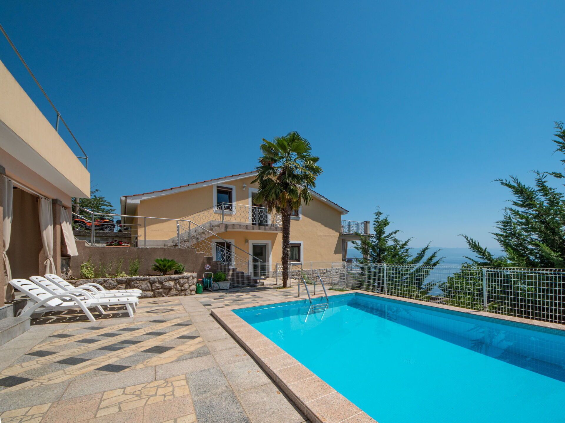 A swimming pool with lounge chairs, a two-story building, and a view of the sea.