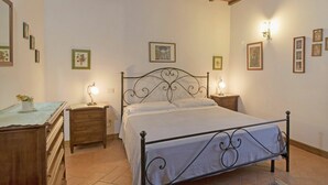 Ein Schlafzimmer mit einem Metallbettgestell, einem hölzernen Schminktisch, Nachttischen mit Lampen und gerahmten Bildern an den Wänden.
